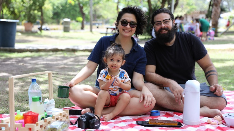 Família sentada sobre toalha de piquenique sorri