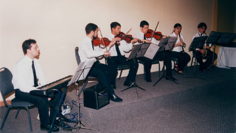 Apresentação da camerata da Unifor em 19 de setembro de 2003. No verso da fotografia, uma dedicatória assinada por Nair Cavalcante de Aguiar: “Nossos agradecimentos aos componentes da camerata da Unifor, Marcus Vinícius, Rodrigo, Adailton, Thiago, Jonathan, Anely e Danilo, pela brilhante apresentação, quando da comemoração do 6º aniversário do Seara Clube da Maturidade de Fortaleza, no salão Iracema do Marina Park Hotel.” (Foto: Acervo Unifor / Restauração digital: Gemini)