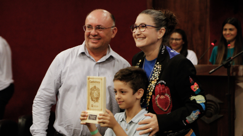 O Vice-reitor de Assuntos Estudantis da Universidade Estadual do Maranhão e filho da homenageada, Paulo Henrique Catunda, e o neto de Dalinha Catunda recebendo o Troféu Cordel Brasileiro da cordelista Paola Torres (Foto: Lucas Sá)