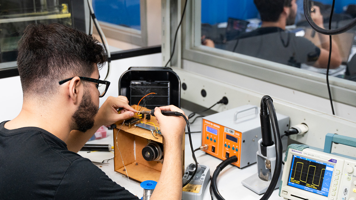 aluno manipula equipamento em meio a computadores