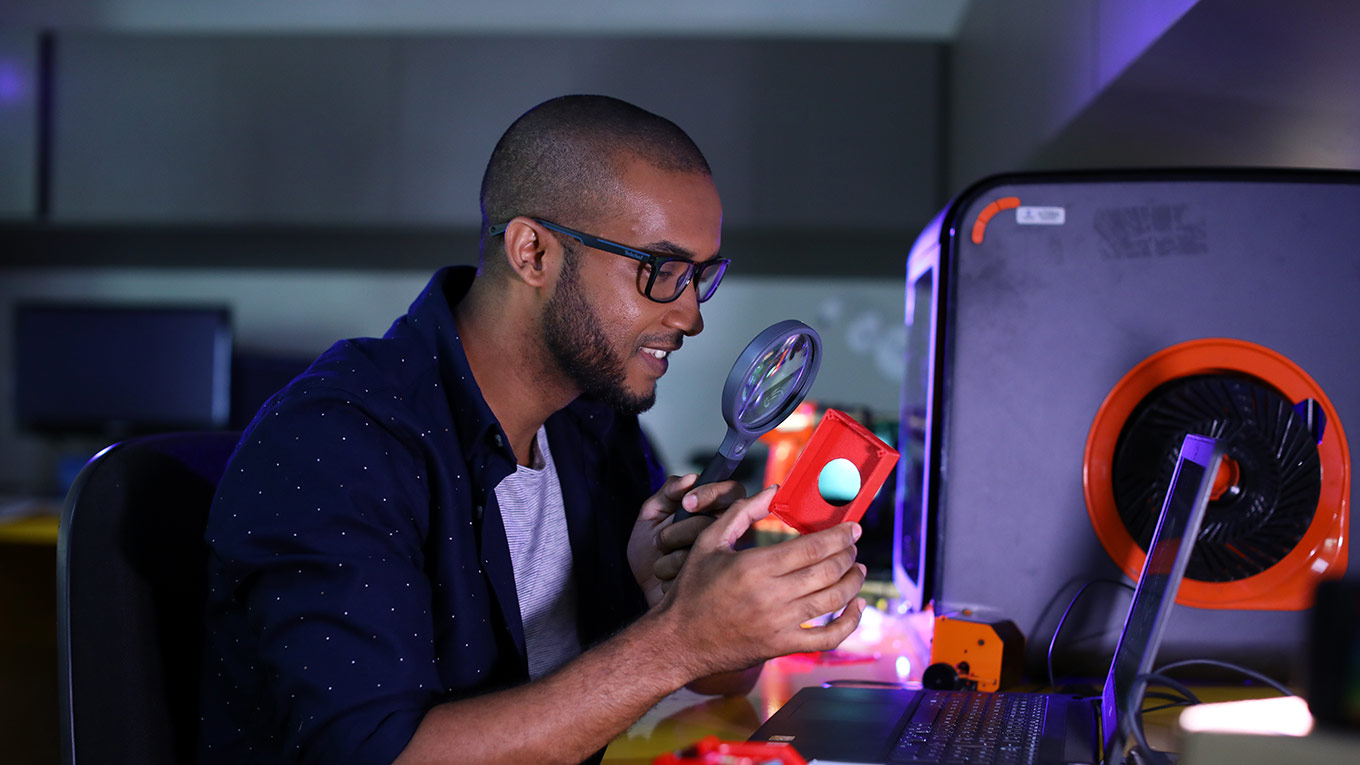 Jovem negro do sexo masculino com uma lupa olhando os componentes de um computador
