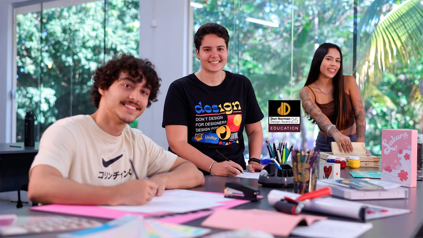 Três jovens manipulam material gráfico sobre uma mesa