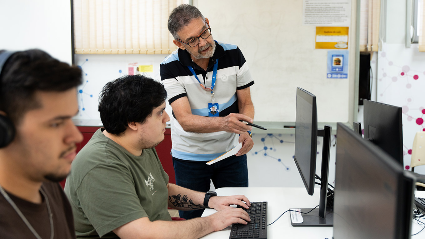 Laboratório de informática com alunos aprendendo ao lado do professor
