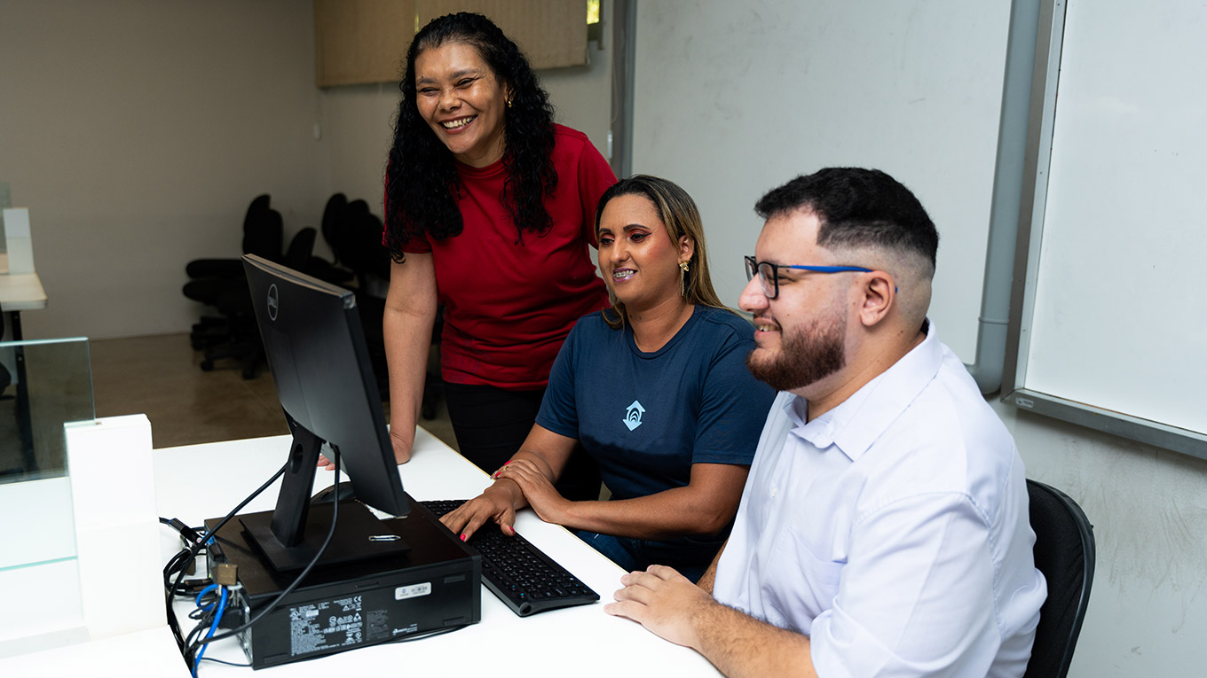Estudantes sorriem junto com a professora em frente a um computador