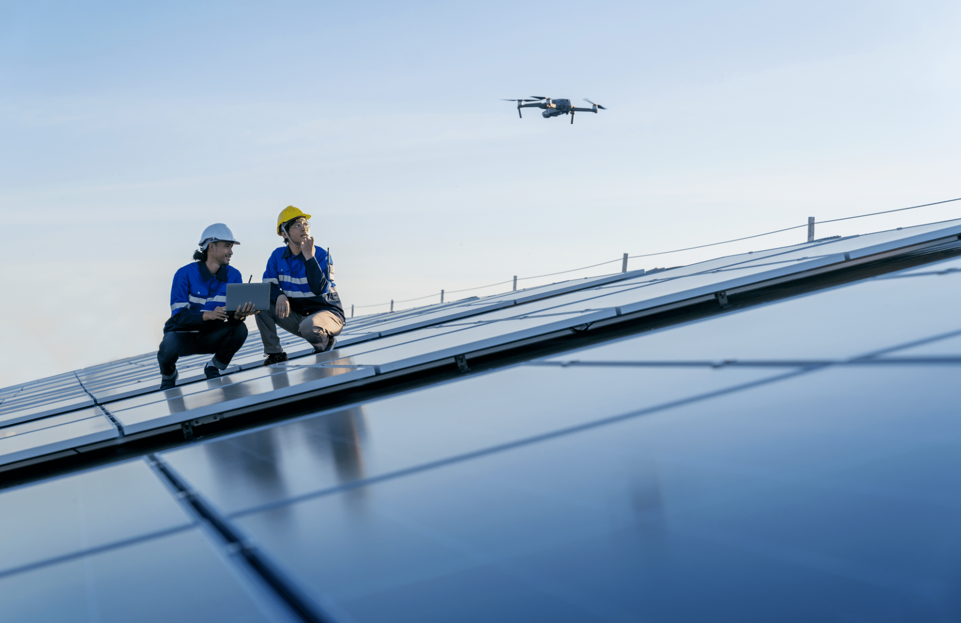 dois engenheiros em cima de um prédio espelhado com um drone no céu