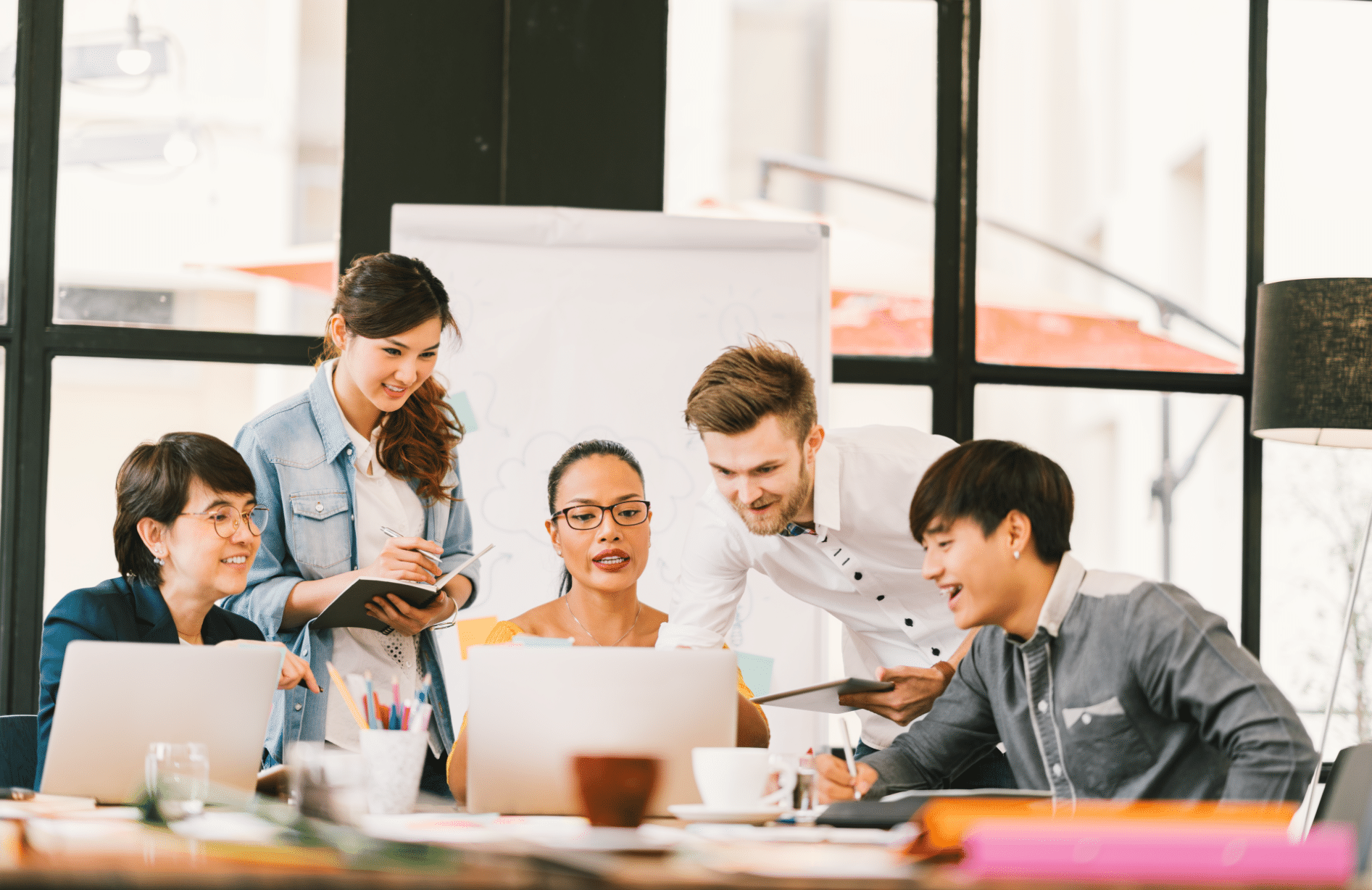 Um grupo de pessoas reunido em uma sala e sentados em uma mesa em frente a computadores discutindo ideias sobre o trabalho