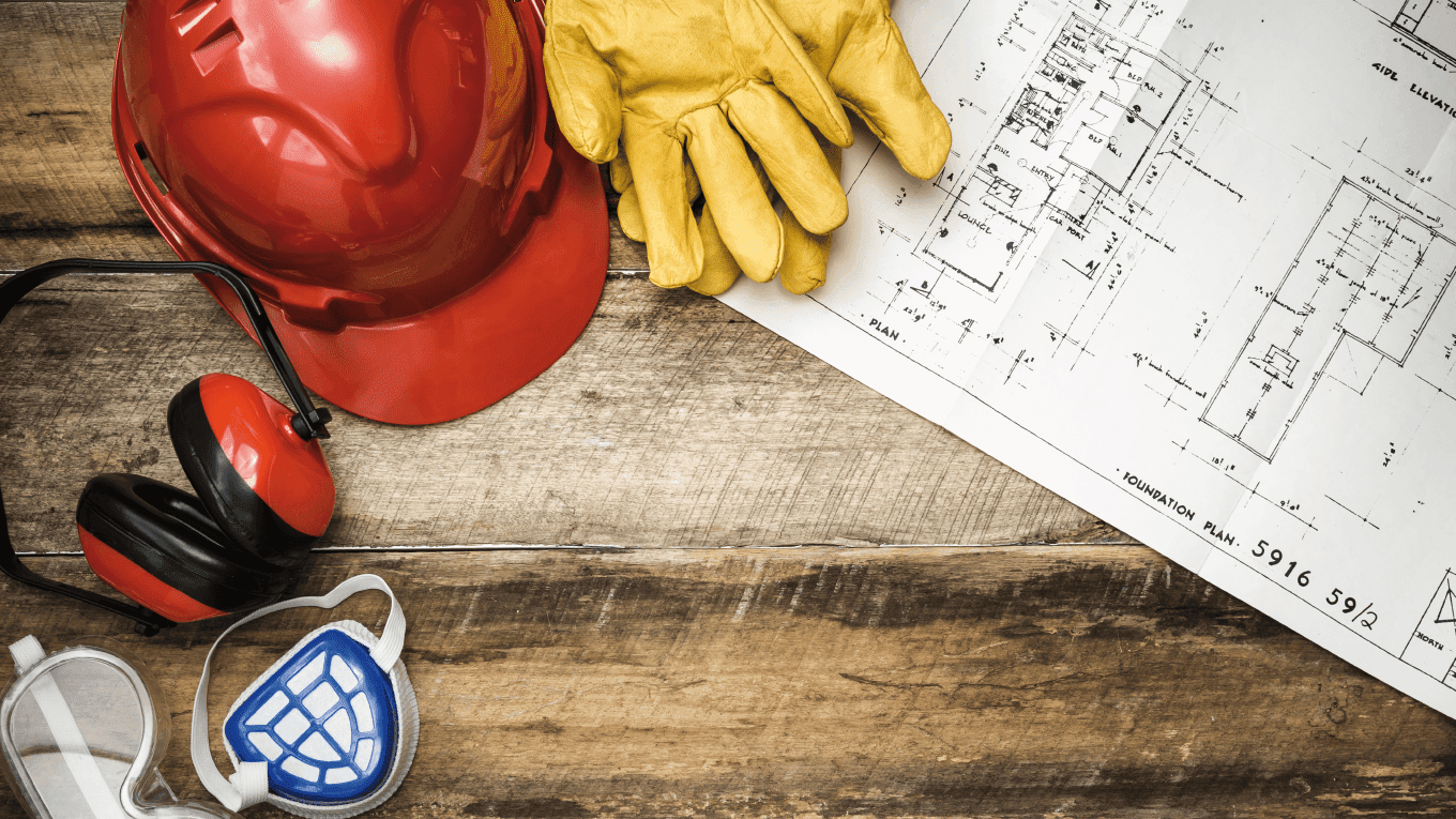 Luvas, projetos e capacete de proteção sobre a mesa.