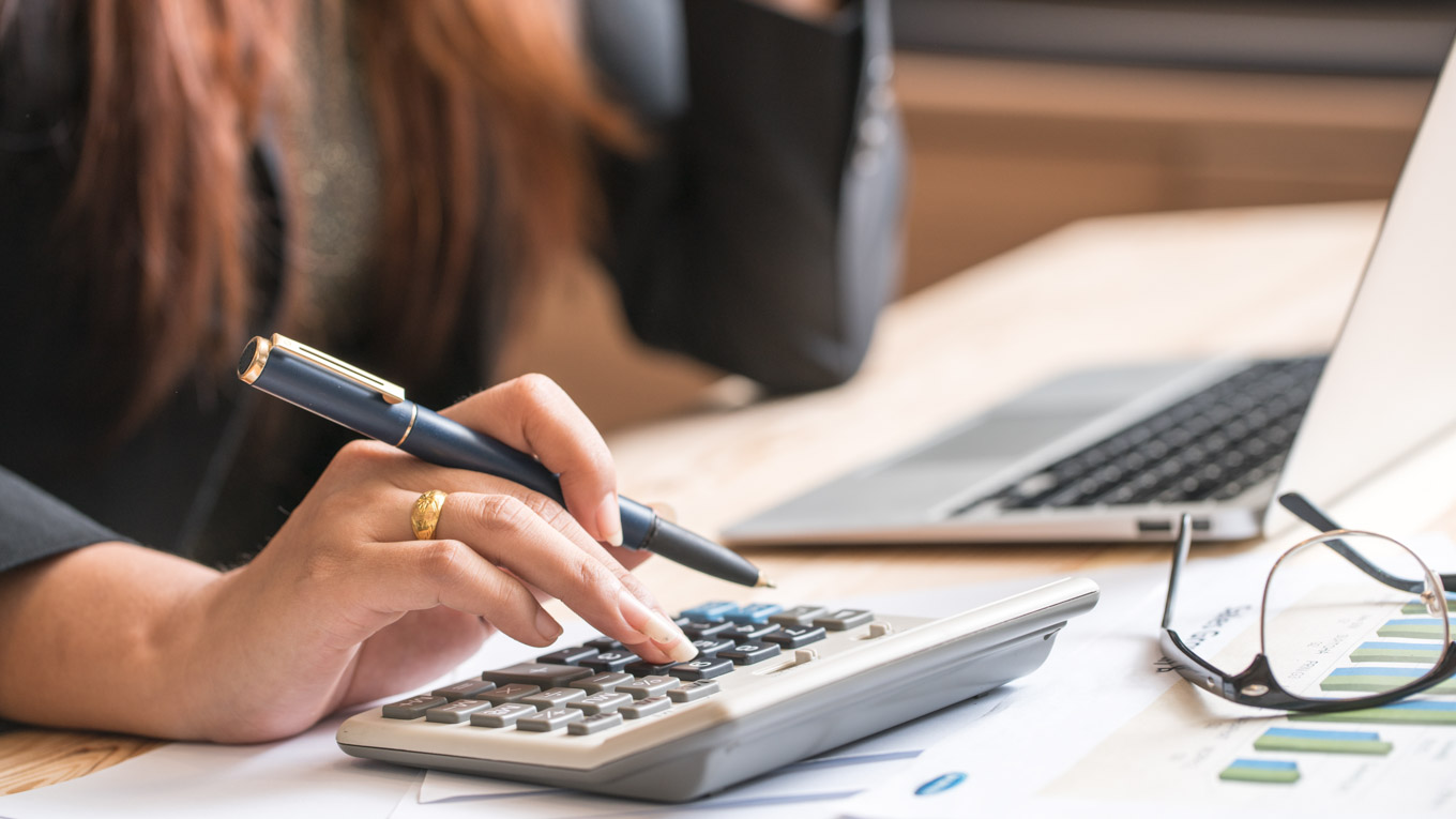 Uma mão feminina em evidência faz cálculos numa calculadora.