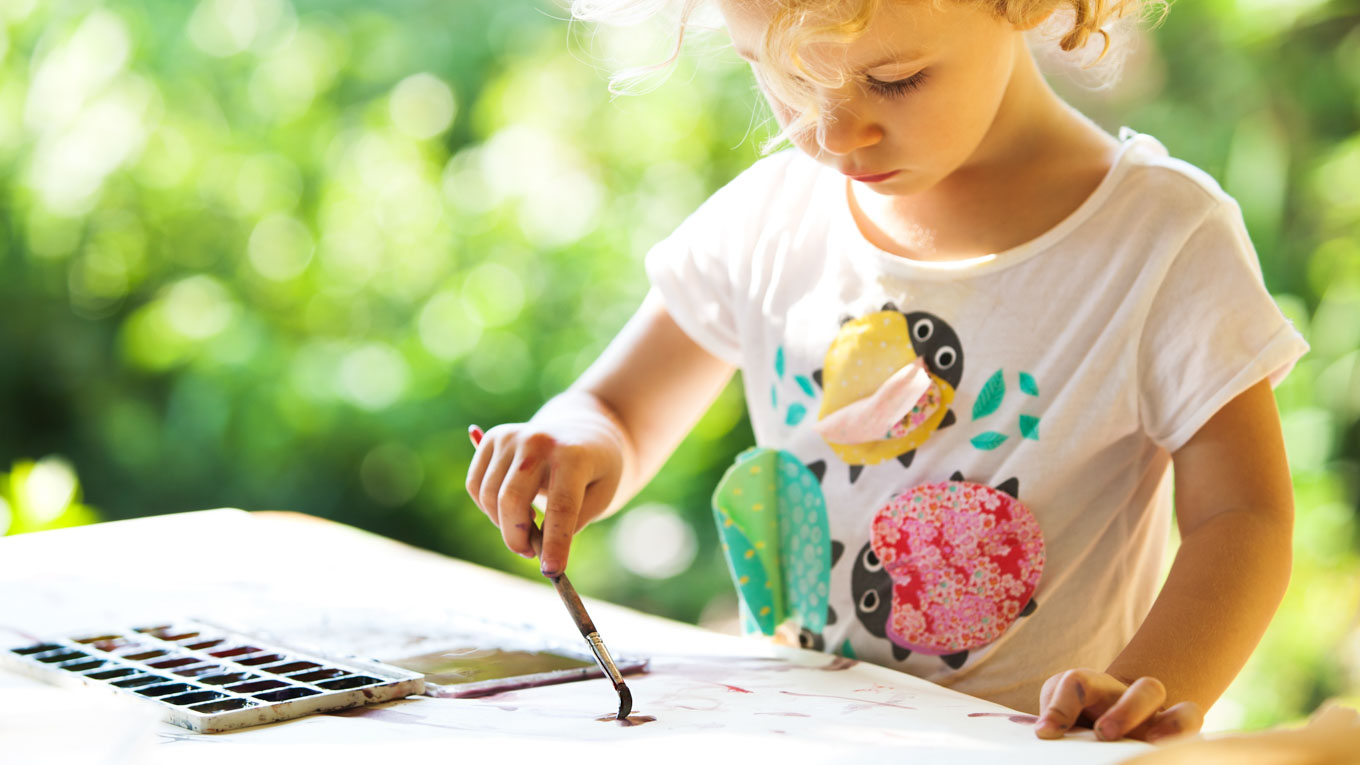 Uma criança está realizando uma pintura com pincel.