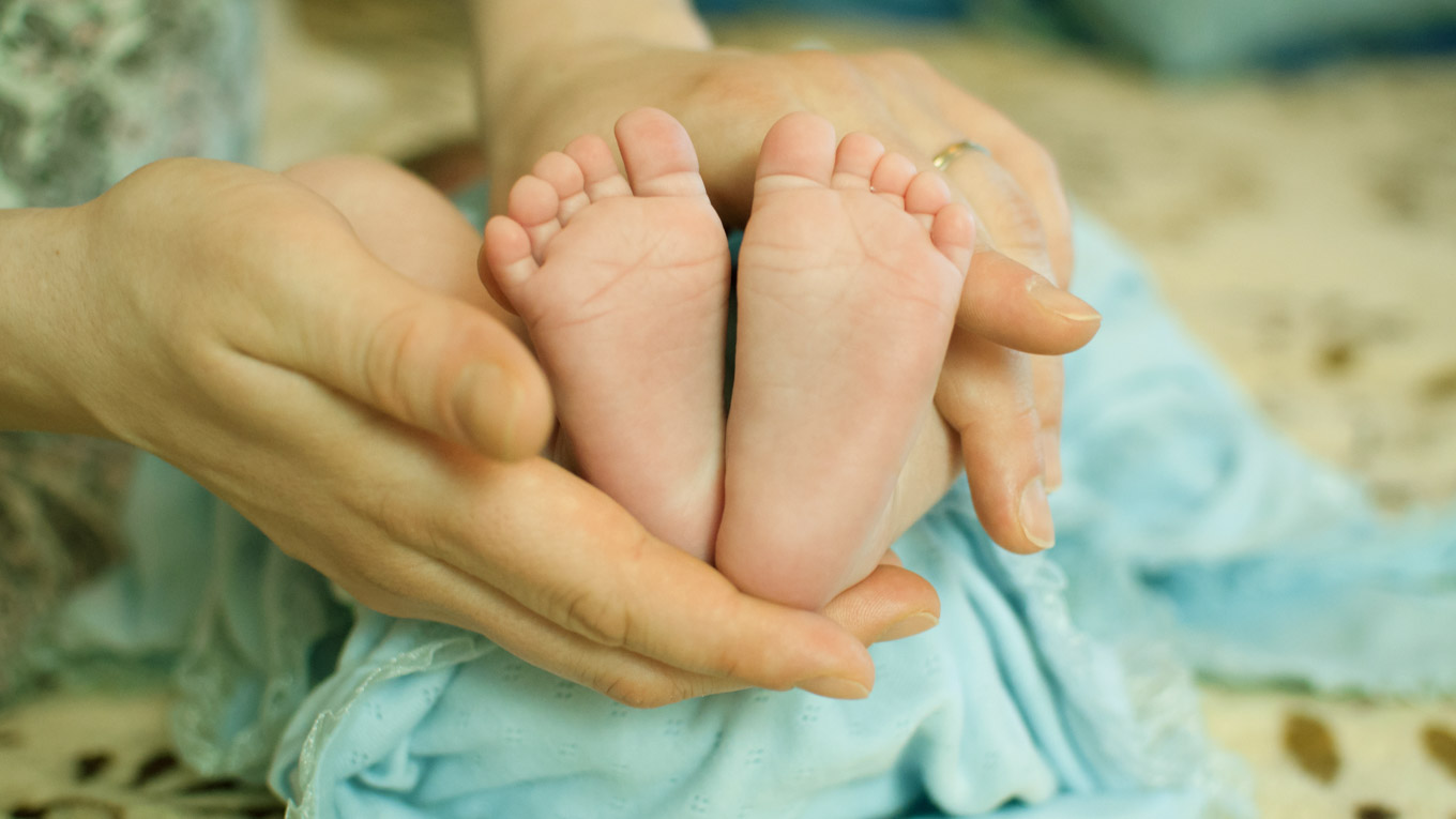 Mãos de adulto seguram os pés de uma criança.