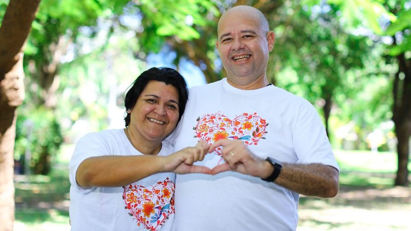 Duas pessoas sorriem enquanto usam suas mãos para formar um coração